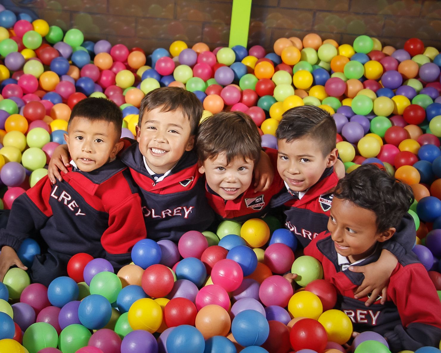 Estudiantes de preescolar de COLREY abrazados y sonriendo en la piscina de pelotas