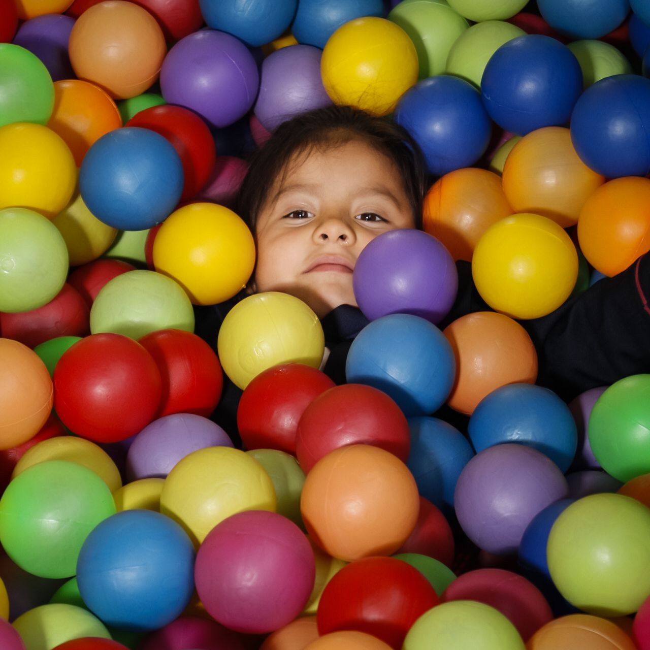 Niña de preescolar asomándose sonriente entre pelotas de colores